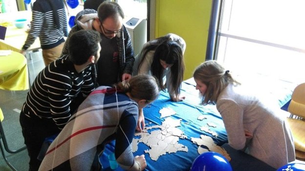 5 Studierende beugen sich über einen Tisch, auf dem ein Europa-Puzzle liegt.