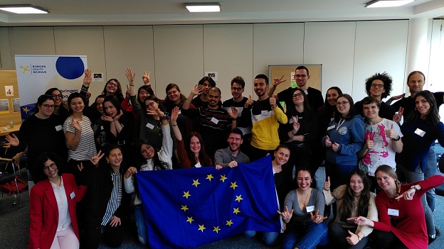 Die Teilnehmer/-innen halten eine EU-Flagge in der Hand und lächeln in die Kamera