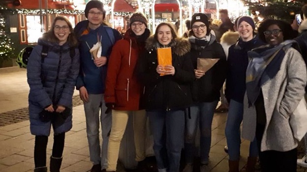 sieben junge Leute stehen aufgreiht auf dem Weihnachtsmarkt in Hamburg und lächeln in die Kamera.