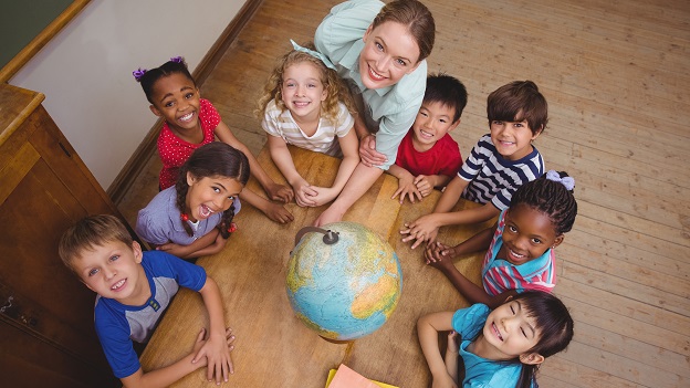 Eine Schulklasse inkl. Lehrerin stehen im Kreis um einen Globus und lächeln in die Kamera