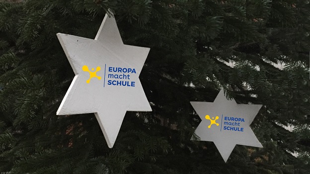 An einem Weihnachtsbaum hängen zwei weiße Holzsterne, auf welchen das EmS-Logo zu sehen ist.