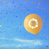 Ein gelber Luftballon fliegt in den Himmel und es regnet Konfetti
