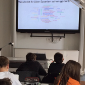 Spanische Studentin steht vor einer Schulklasse in München und zeigt eine Präsentation