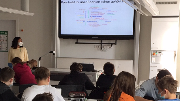Spanische Studentin steht vor einer Schulklasse in München und zeigt eine Präsentation