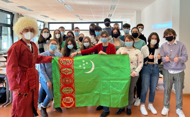 Zusammen mit einem turkmenischen Studenten lächelt eine Schulklasse in die Kamera.