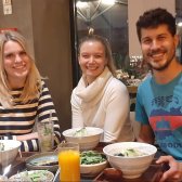 Drei junge Menschen lächeln und sitzen gemeinsam an einem Tisch mit Essen