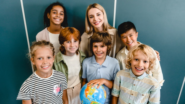 SchülerInnen lächeln mit der Lehrkraft in die Kamera und halten einen Globus
