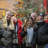 Ehrenamtliche des Programms Europa macht Schule stehen auf dem Christkindlmarkt in Regensburg und posieren vor einem Weihnachtsbaum
