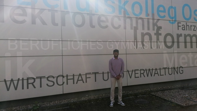 Person steht vor dem Logo einer Schule (Berufskolleg Ost).