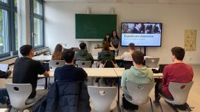 Auf dem Bild sieht man zwei Studentinnen aus Spanien, die vor einer Schulklasse stehen und eine Präsentation über die Erinnerungskultur in Spanien und Deutschland zeigen.
