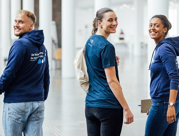 3 Studierende bekleidet mit dem "Europa macht Schule" Hoodie laufen durch die Hochschule auf der Suche nach neuen Engagierten für EmS